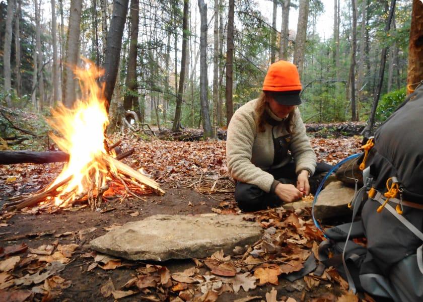 Woman sitting on ground in forest with fire to her left
