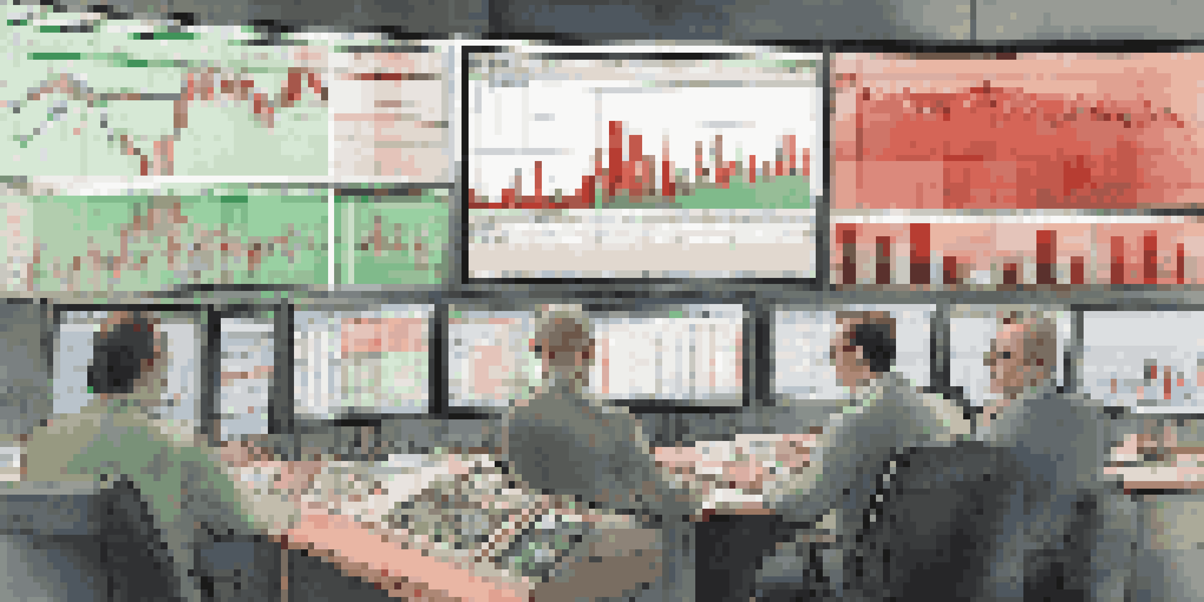 A stock market trading desk with monitors showing fluctuating graphs and charts in warm light.