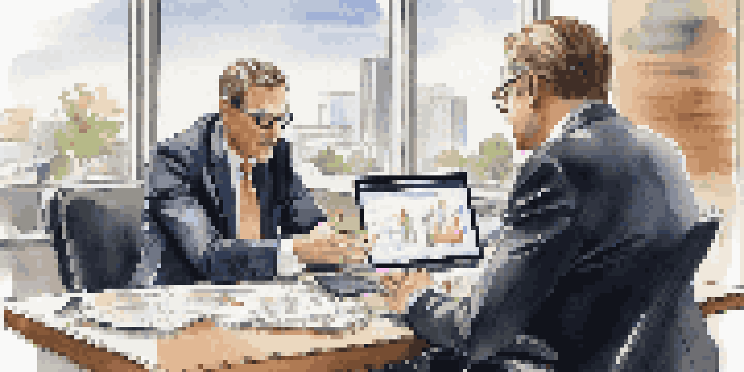 A financial advisor discusses investment strategies with a client in a bright office, highlighting charts on a laptop.