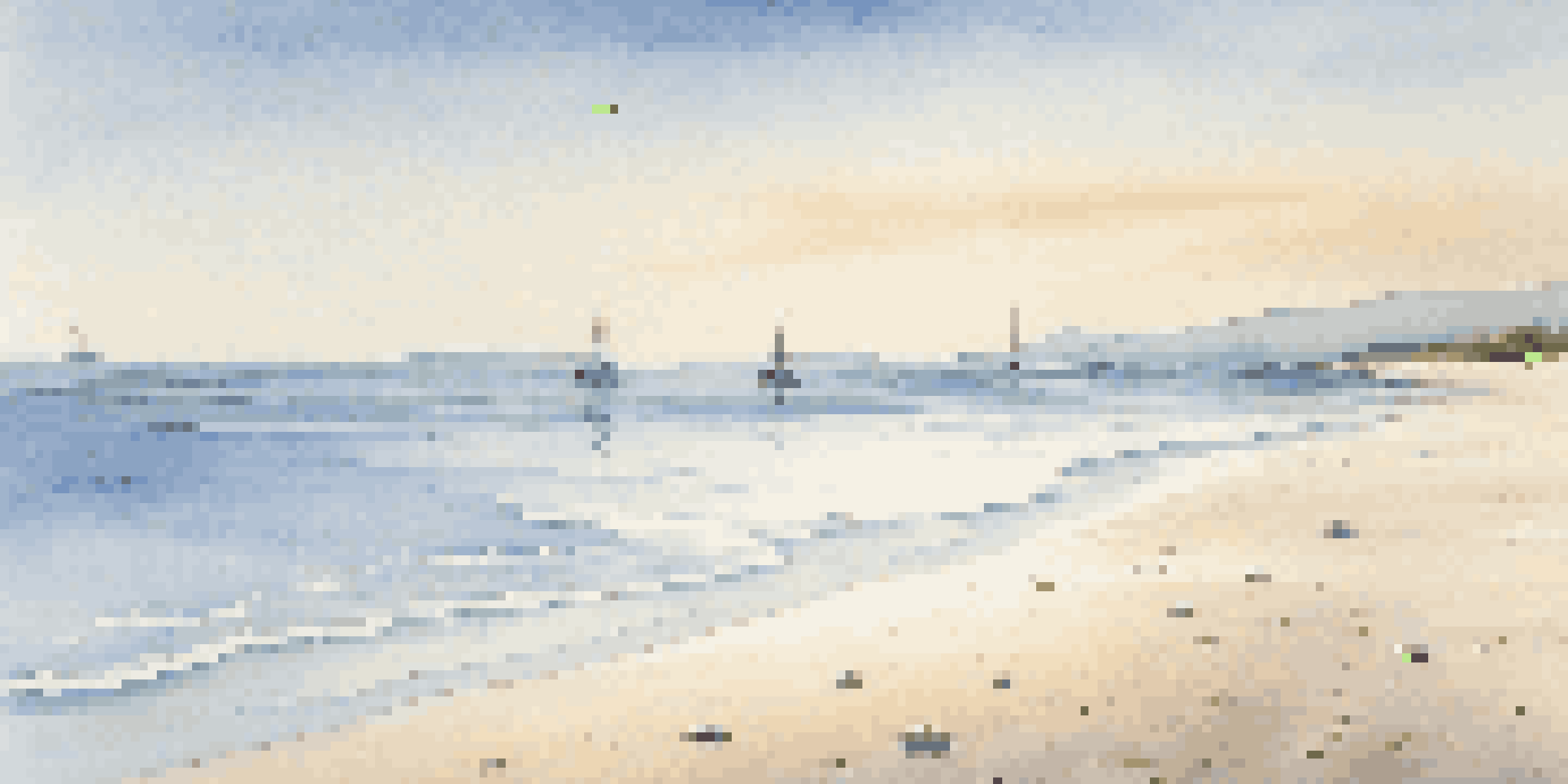 A peaceful beach scene with calm ocean waves, a clear blue sky, and distant sailboats on the horizon.