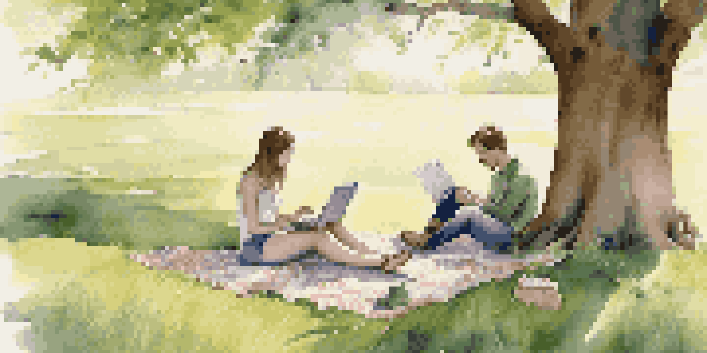 A young couple sitting on a picnic blanket under a large tree, looking at their finances with a laptop and notebooks, in a green outdoor setting.