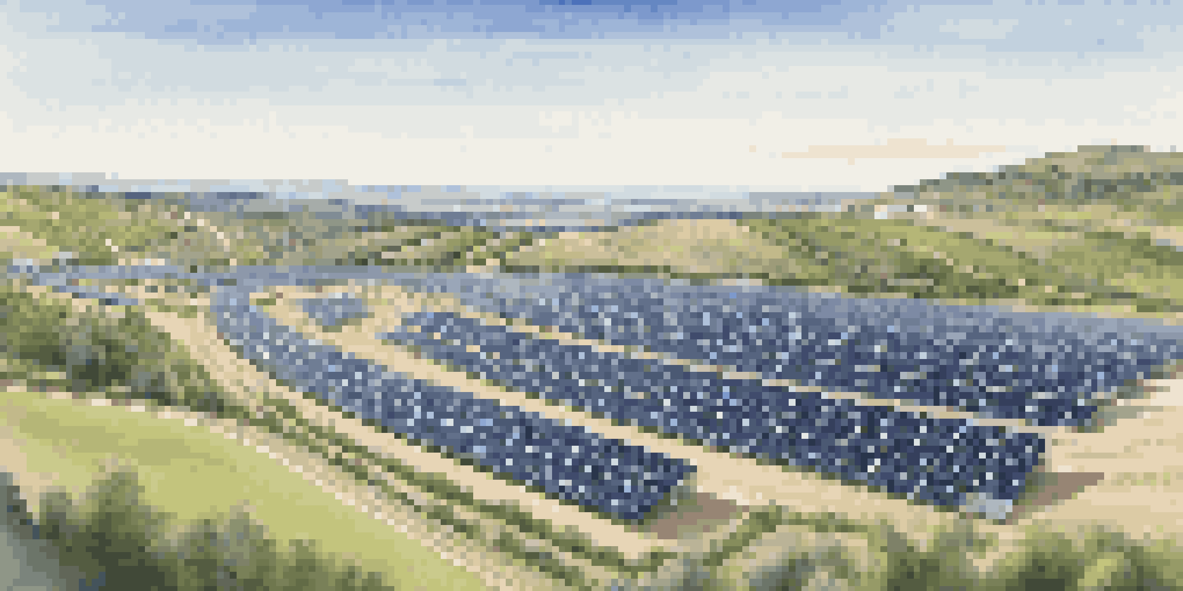 A solar farm with rows of solar panels under a blue sky, surrounded by green hills and a winding road.