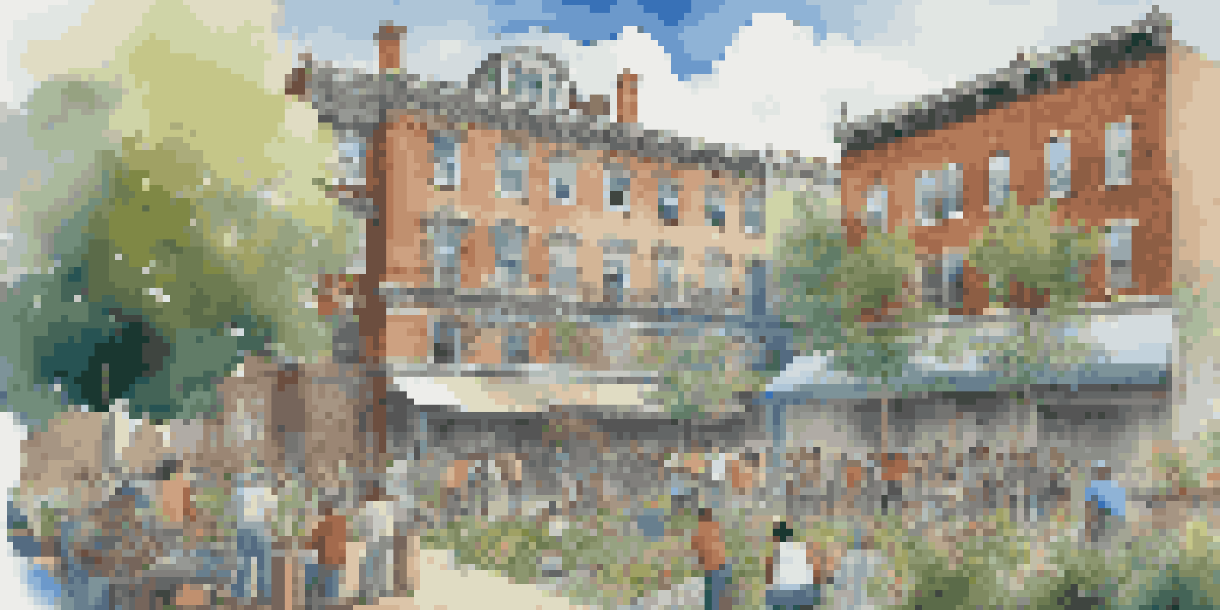 A group of diverse community members collaborating on a mural painting in front of a historic building under restoration, surrounded by greenery and flowers.