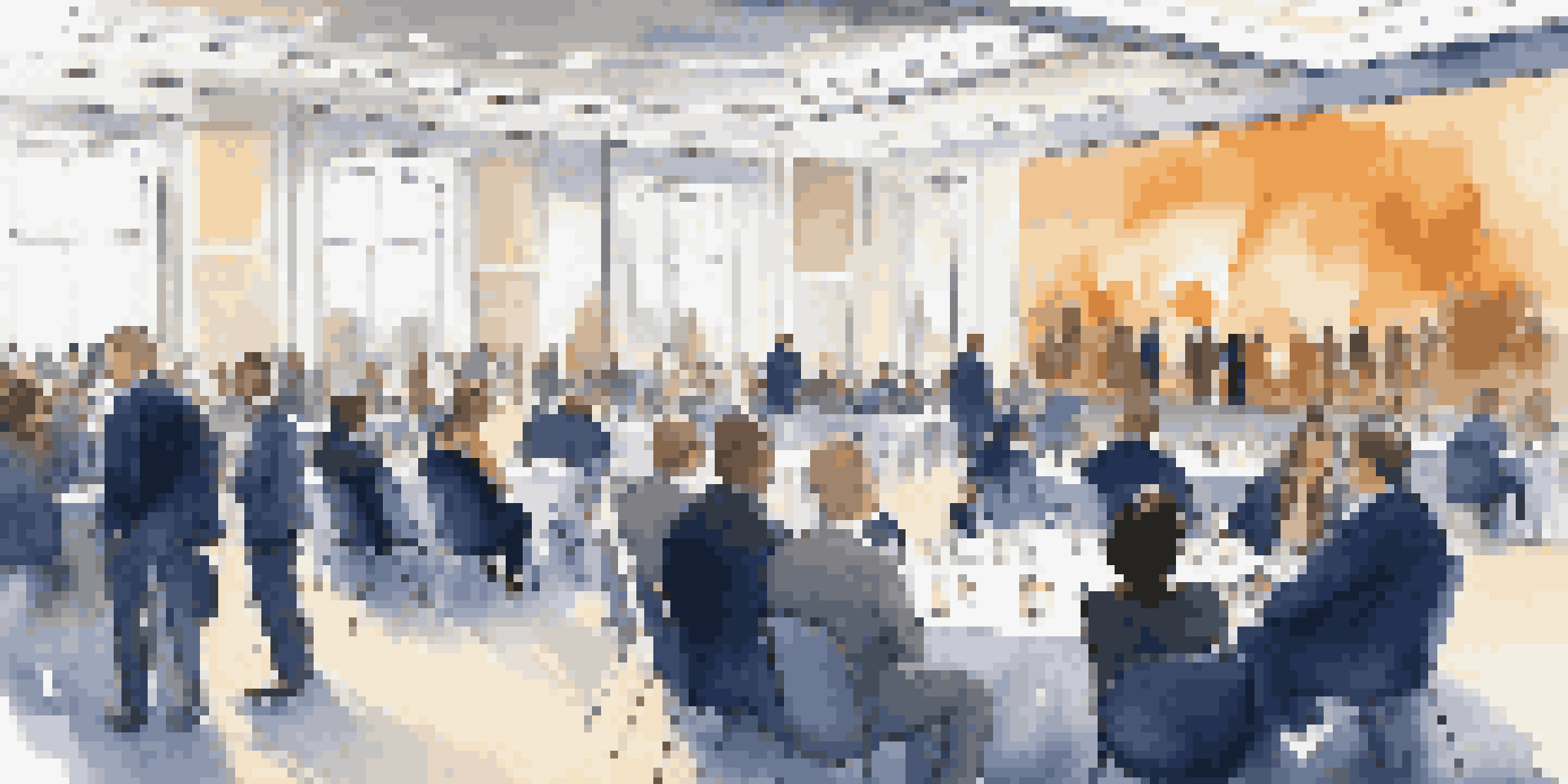 A networking event with professionals in formal attire engaged in conversation in a conference hall.