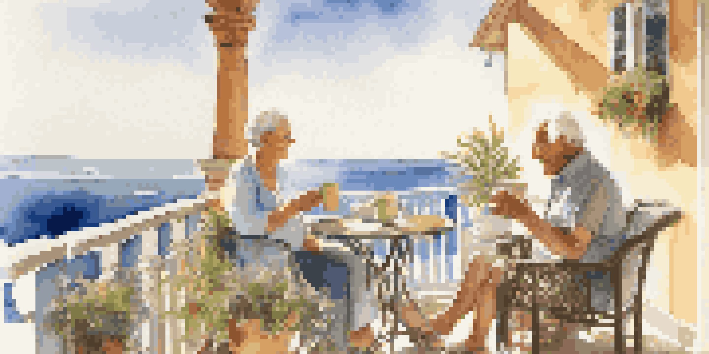 An older couple sitting on a balcony, smiling and enjoying coffee with an ocean view.