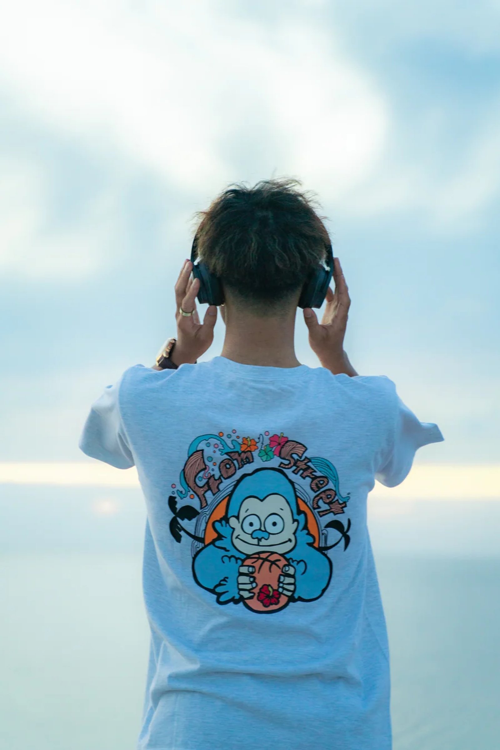 ヘッドホンをつけ、ゴリラのバックプリントTシャツを着た後ろ姿