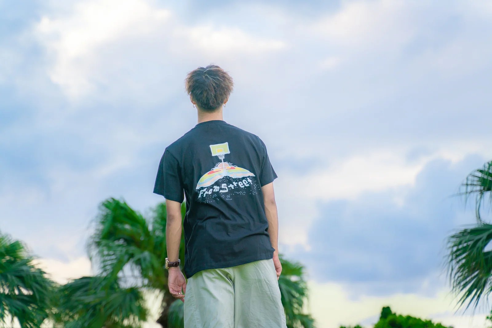 青空の下でFrom StreetのバックプリントTシャツを着た後ろ姿