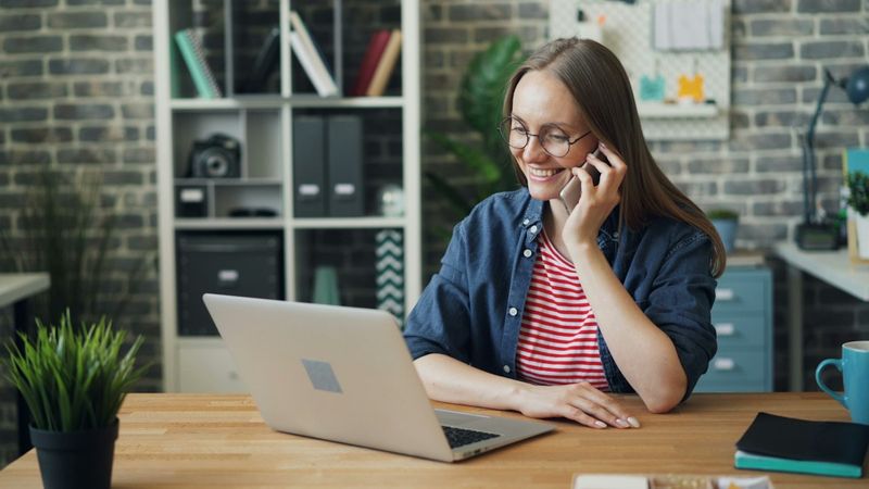 A woman talking on her phone while using a laptop