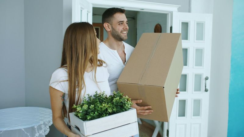 Two people carrying moving boxes into a new home