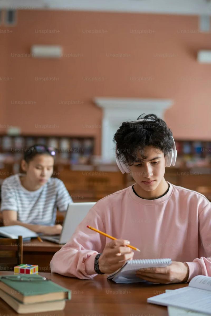 헤드폰을 끼고 노트를 보며 강의를 복습하는 대학생