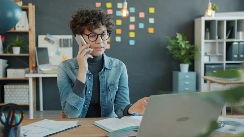 A woman on a customer service call at a desk with an open laptop