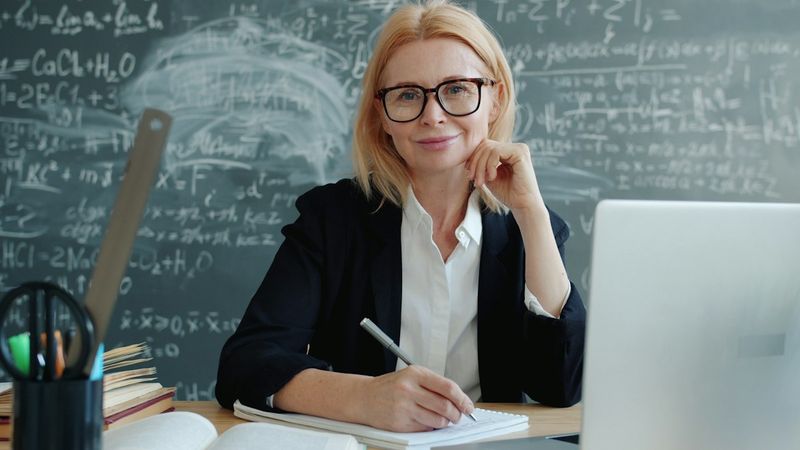 A smiling teacher sitting at a desk with a laptop