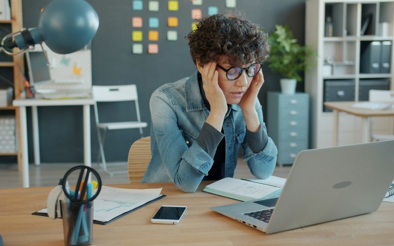 Office worker holding their head in frustration in front of a laptop