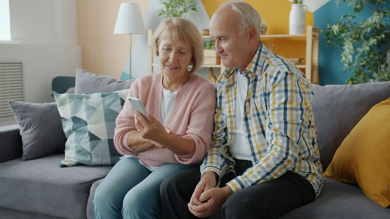 An elderly couple sitting on a couch looking at a smartphone together