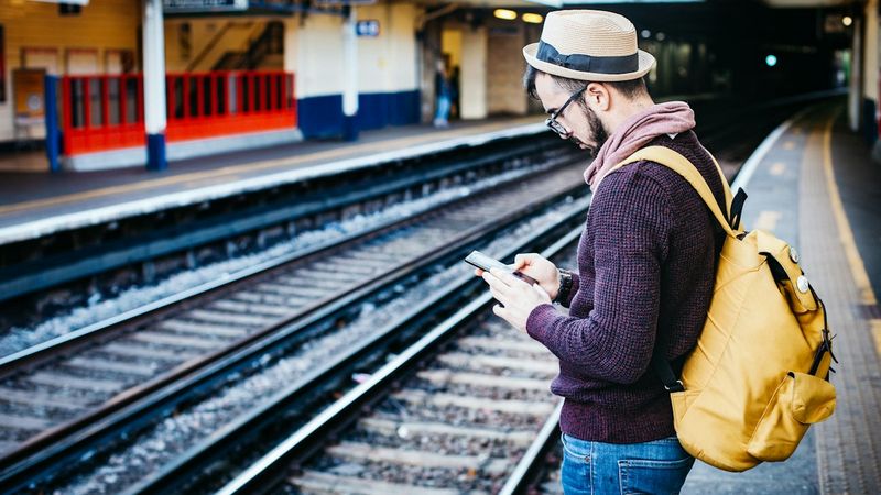 A traveler looking at a phone in front of train tracks