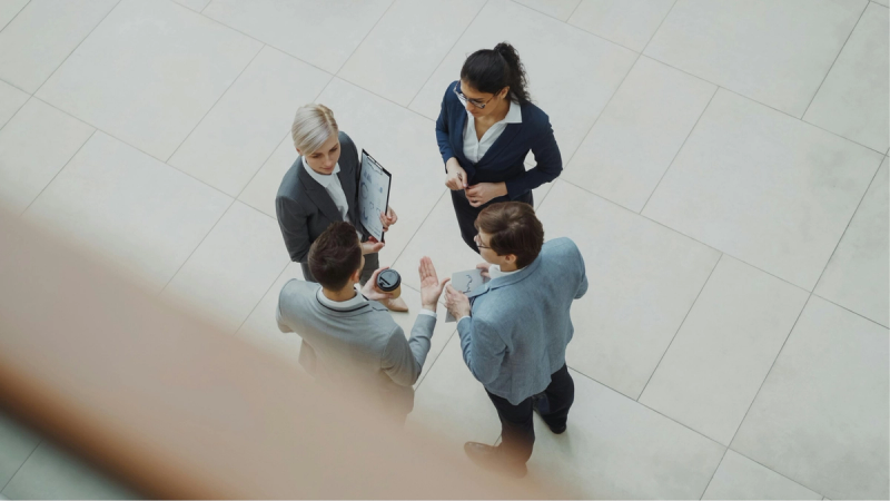 Overhead view of four business professionals in formal attire discussing documents and ideas in a modern office setting.