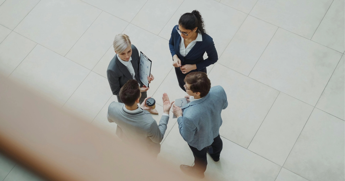 Overhead view of four business professionals in formal attire discussing documents and ideas in a modern office setting.