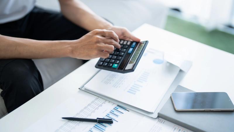 A person sitting at a white desk using a calculator.