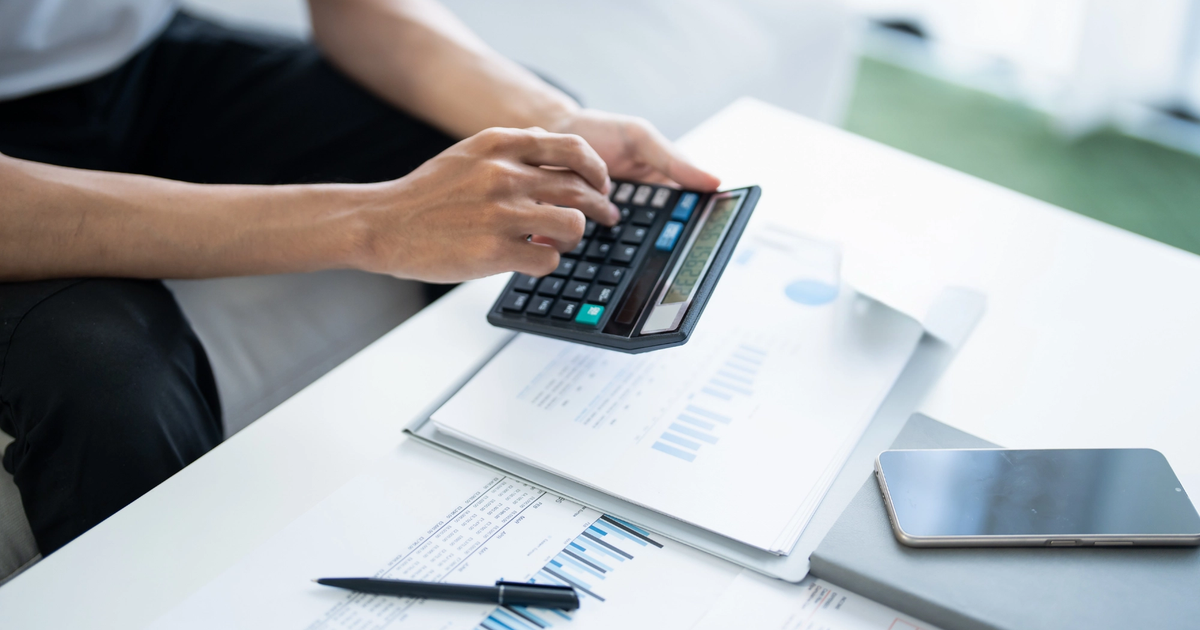 A person sitting at a white desk using a calculator.