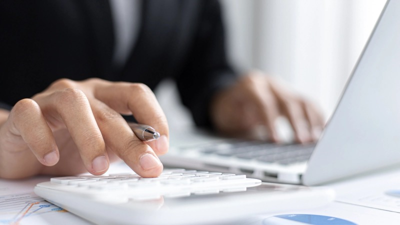 Close-up of an SME owner using a calculator and laptop to prepare for business funding.