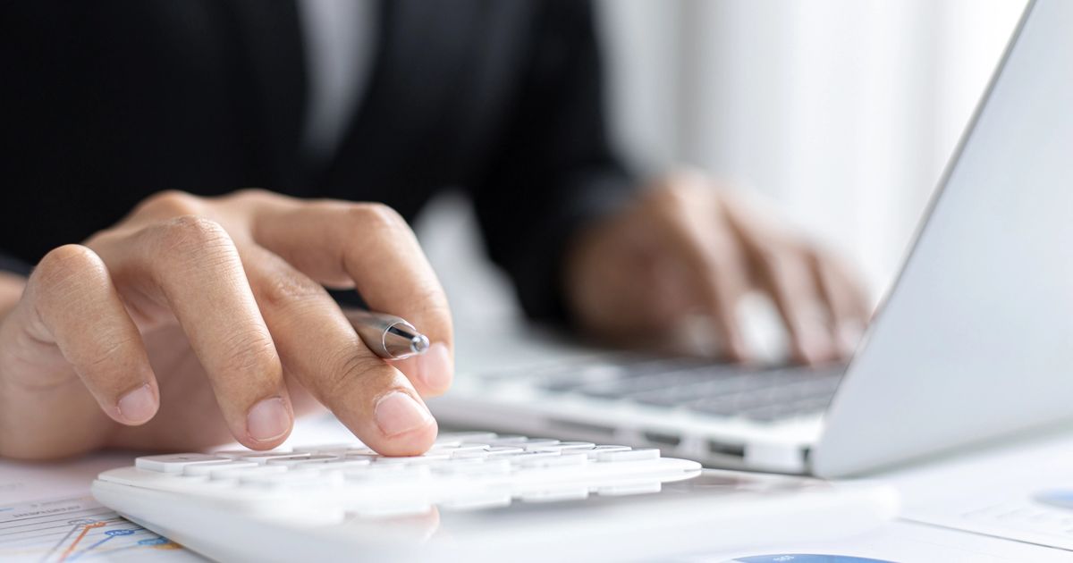 Close-up of an SME owner using a calculator and laptop to prepare for business funding.