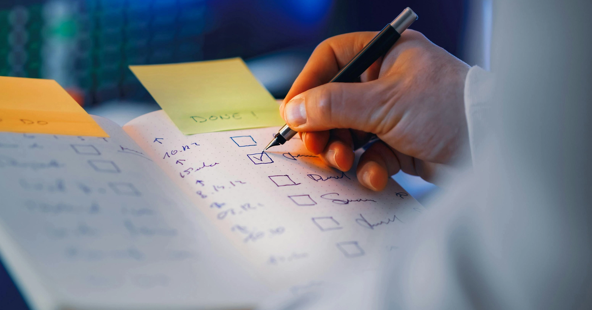 Lender writing a checklist for a commercial loan in a notebook with sticky notes visible in the background.