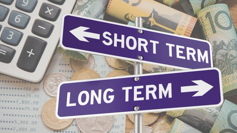 Directional sign showing short-term and long-term choices over a background of cash, coins, and a calculator, representing business financing decisions.