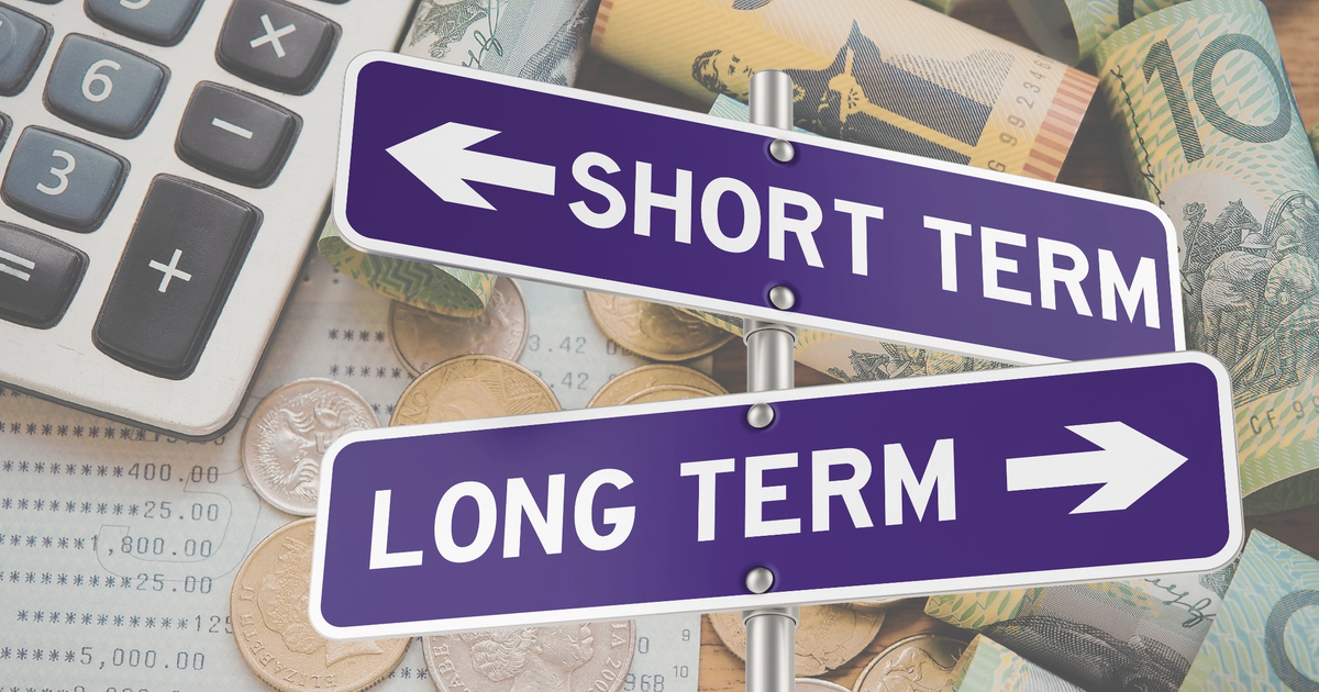 Directional sign showing short-term and long-term choices over a background of cash, coins, and a calculator, representing business financing decisions.