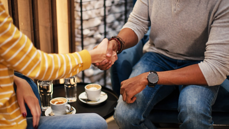 Close-up of professionals shaking hands at a table while discussing how to refinance their business loans.