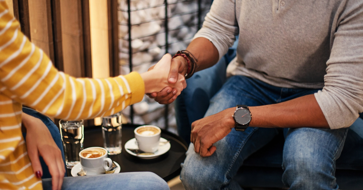 Close-up of professionals shaking hands at a table while discussing how to refinance their business loans.