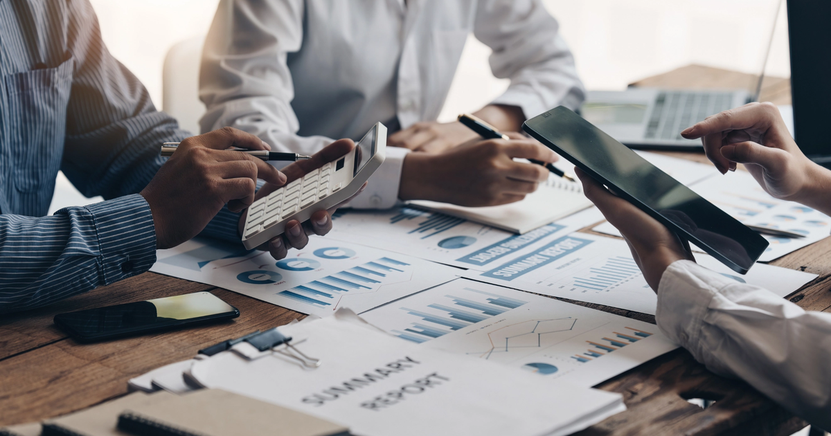 Two business professionals sitting at a desk reviewing financial documents, spreadsheets, and a calculator during a business meeting.