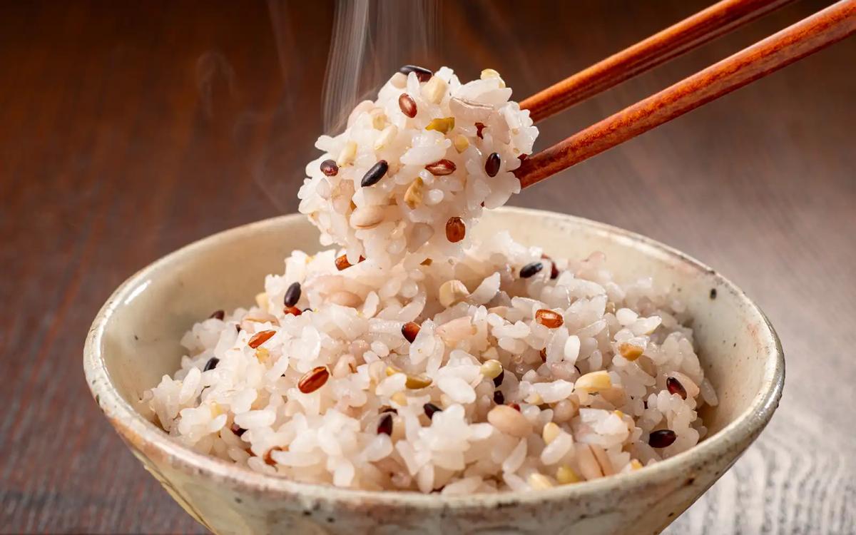 Mixed grain rice with red beans and goji berries held by chopsticks over bowl
