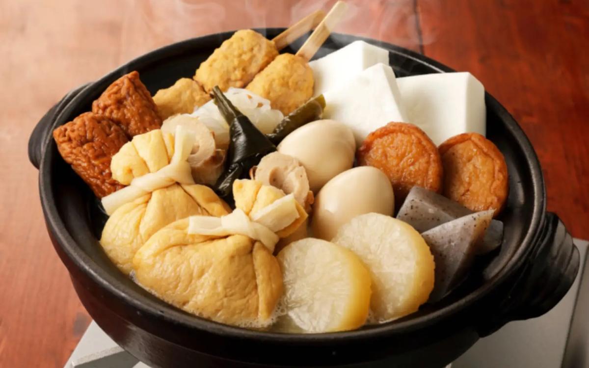 Hot pot with fish cake, tofu, mushrooms, and vegetables in black ceramic bowl