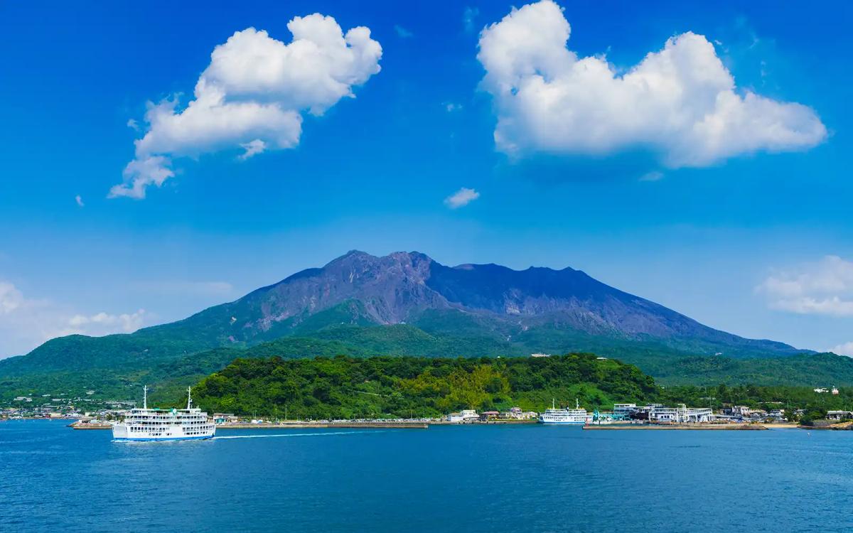 Sakurajima volcano with coastal town and ferry boat under blue sky