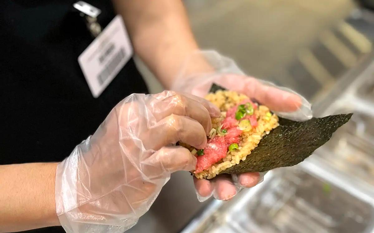 Gloved hand holding sushi roll with colorful toppings at food event