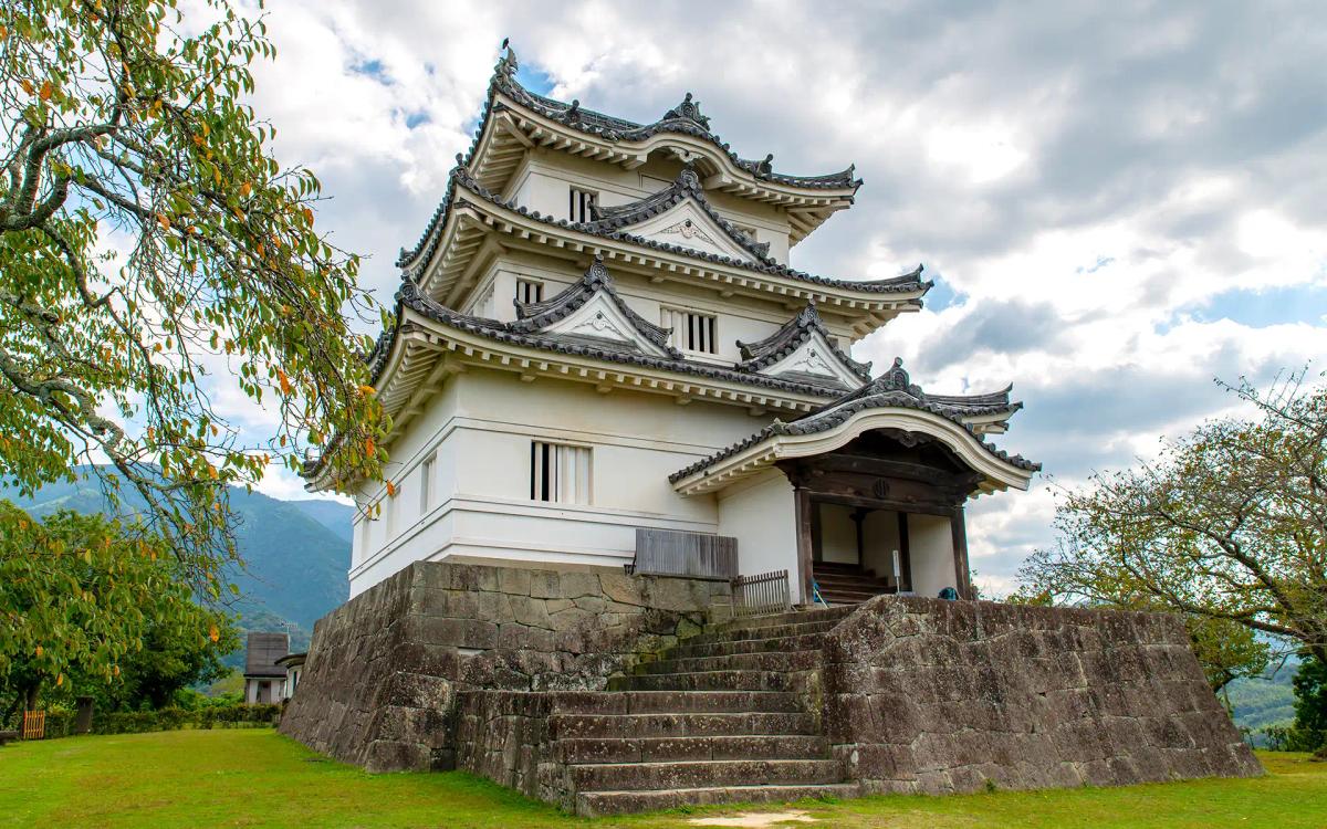 Traditional Japanese castle with multiple tiered roofs, stone foundation, surrounded by green landscape