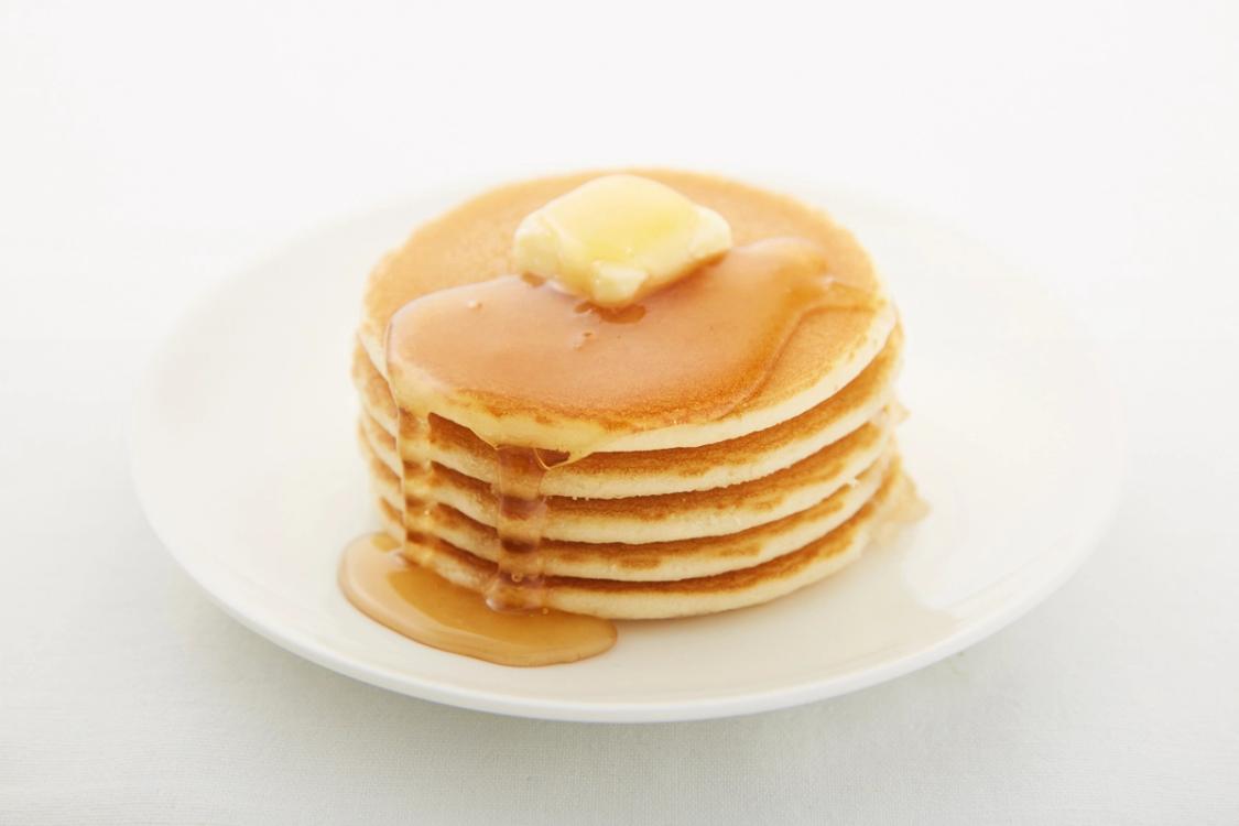 Stack of golden pancakes with butter and syrup on white plate