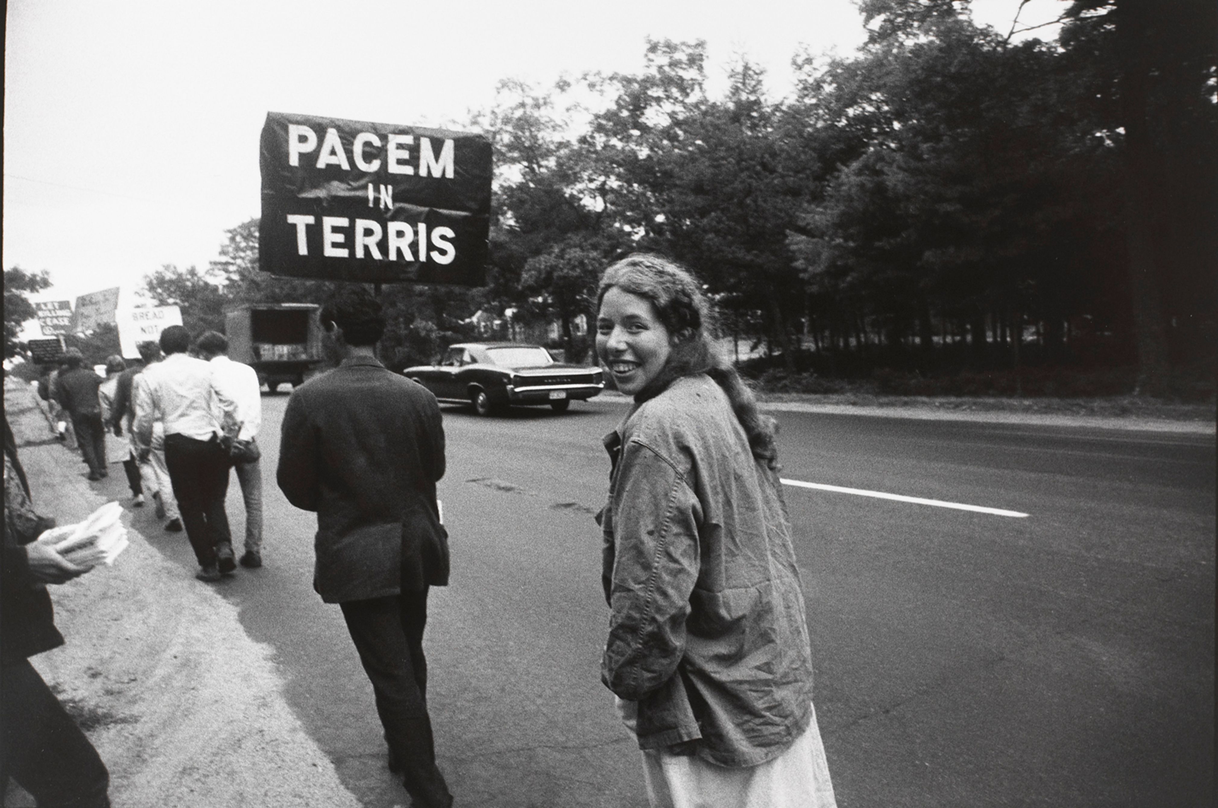 Untitled (Woman walking behind a sign “PACEM TERRIS”, smiling back at camera)