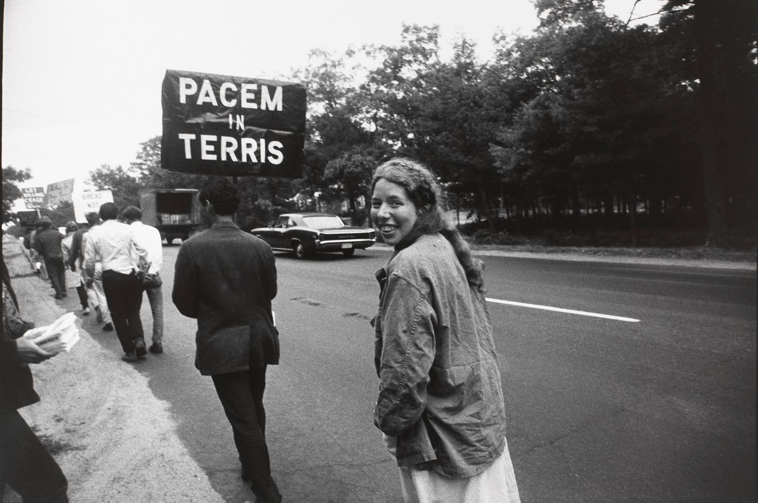 Untitled (Woman walking behind a sign “PACEM TERRIS”, smiling back at camera)