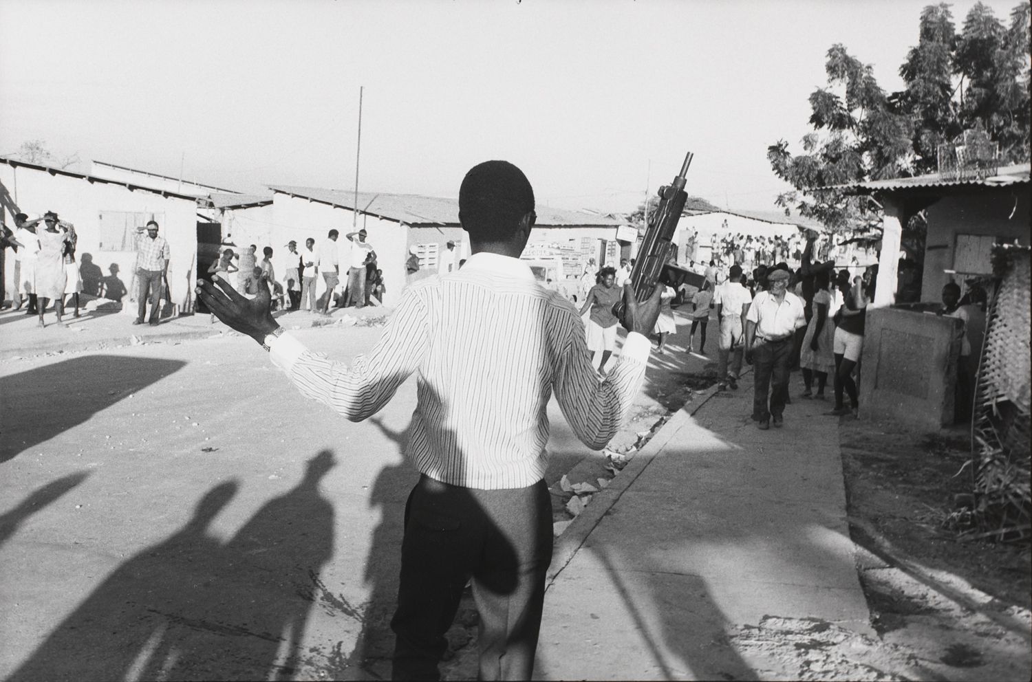An out-of-uniform Tonton Macoute with an Uzi machine gun harasses a crowd