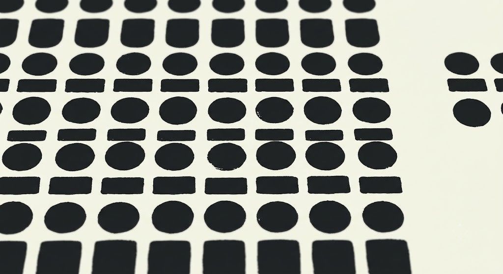 Close-up pattern of repeating black dots and bars on a cream background, representing standardised, commoditised output.