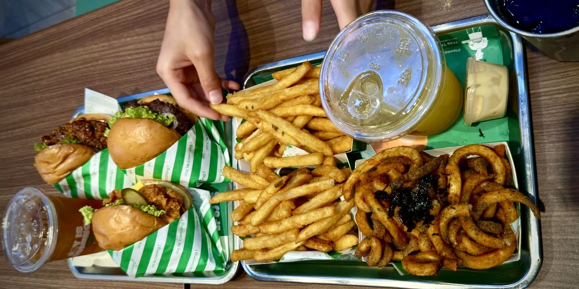 Two trays of chicken burgers, seasoned fries and nori twisty fries on a food court table in Malaysia.