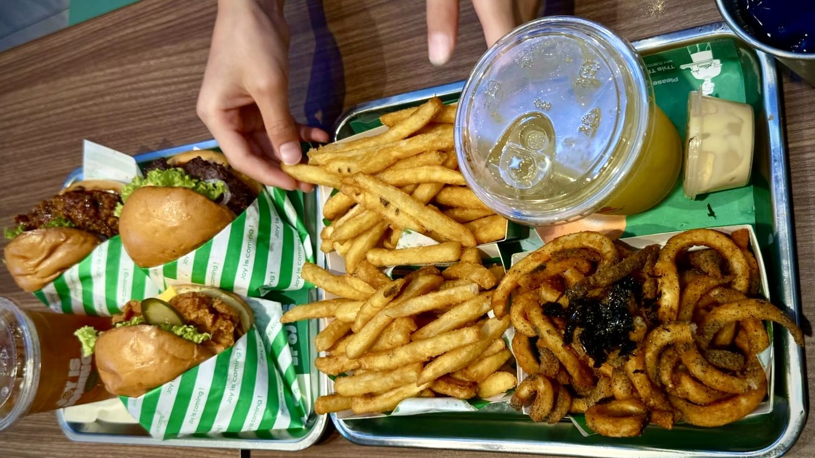 Two trays of chicken burgers, seasoned fries and nori twisty fries on a food court table in Malaysia.