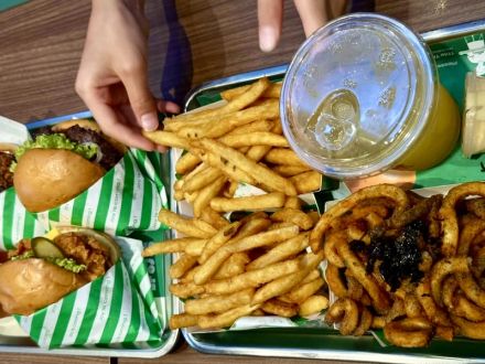 Two trays of chicken burgers, seasoned fries and nori twisty fries on a food court table in Malaysia.