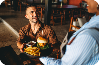 Server gave burger and fries to a man at a table, framed by dining-themed Visa award cards.