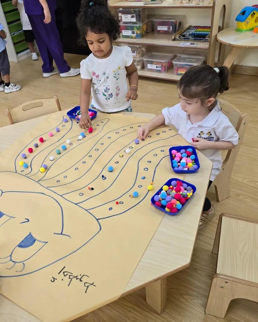 Two toddlers sorting colourful pom-poms at an activity table