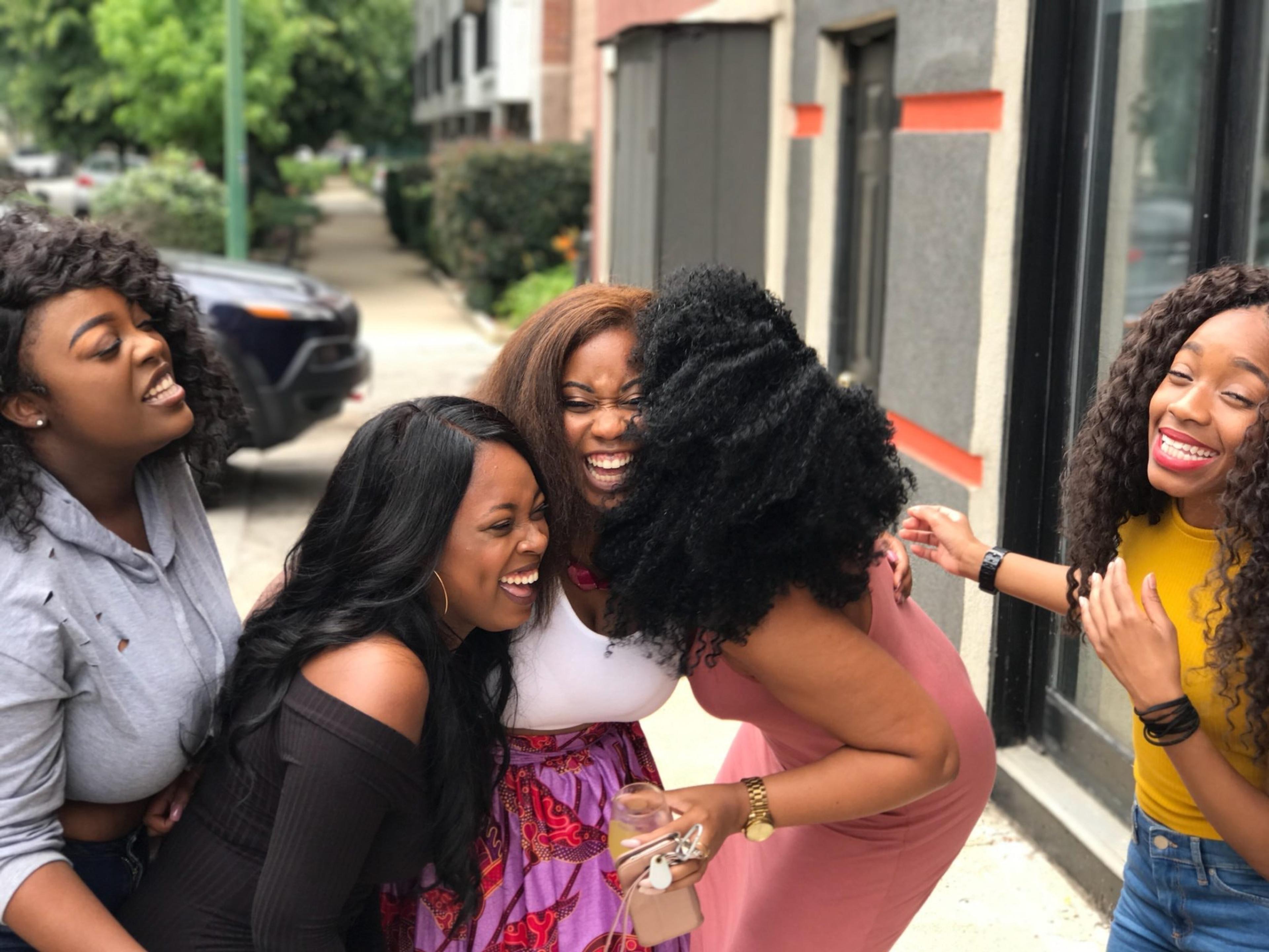 A group of Black women laughing and hugging on a sidewalk