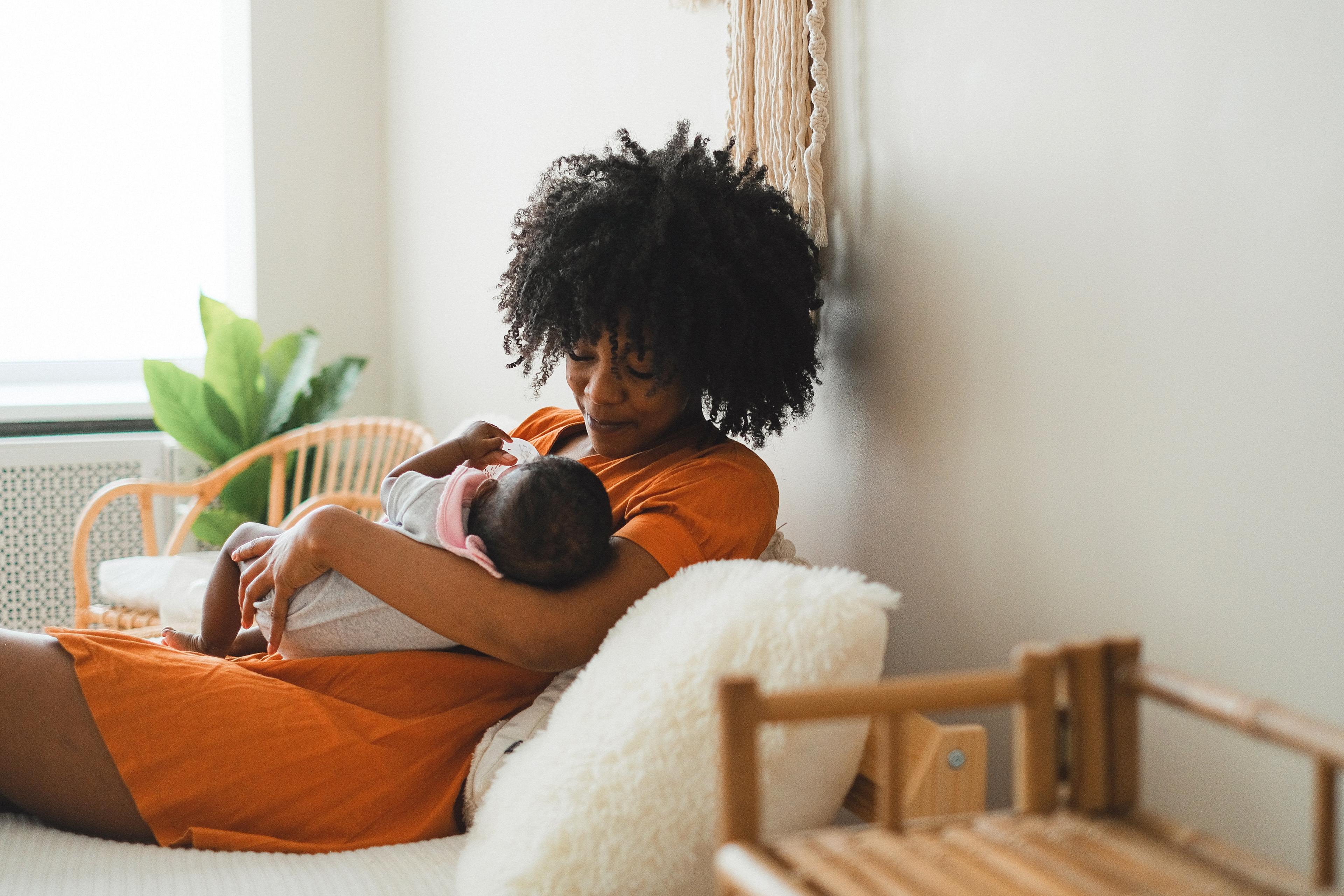 A black mother sits in a chair holding her newborn child