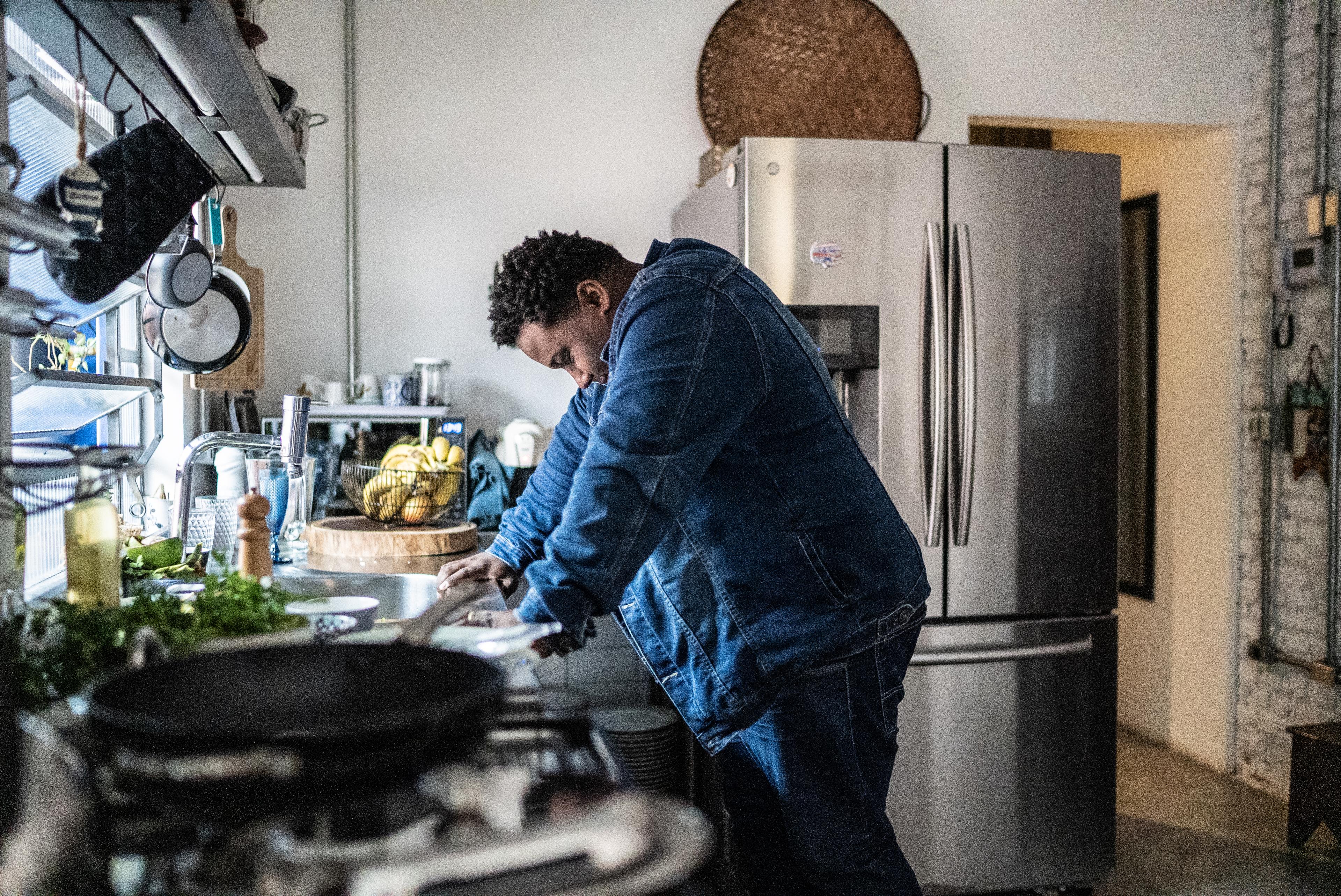 A man stands over a sink in a kitchen looking upset