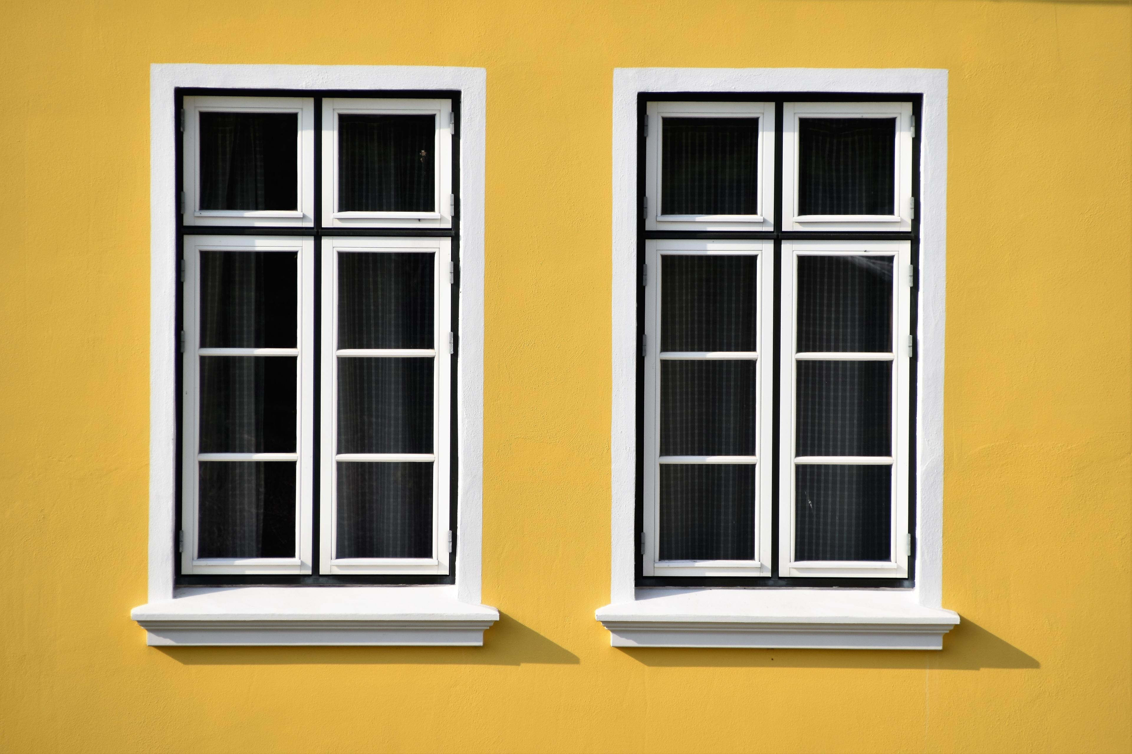 Two black windows with white trim against a yellow wall
